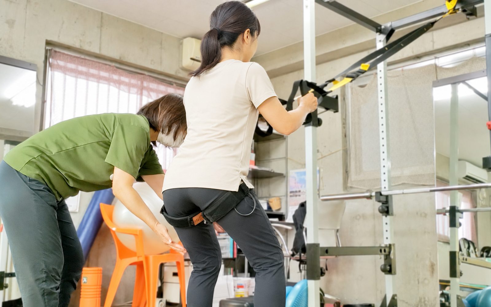 トレーナーが見守るなか、利用者がTRXサスペンショントレーナーを使ってトレーニングするMKジムの風景