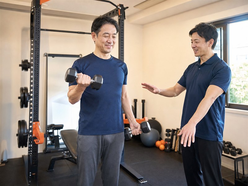 40代男性がトレーナーの助言を受けながらダンベル運動をするAI生成のテーマ写真